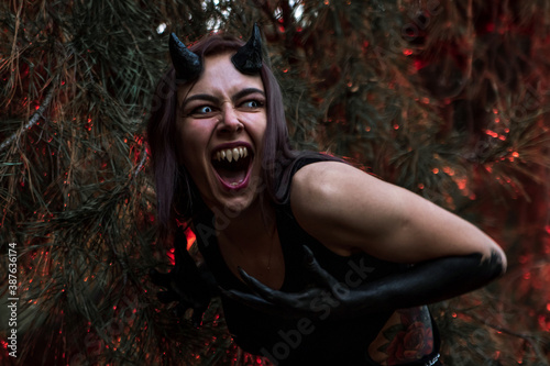 Fotografía a girl with fangs and horns obsessed with evil screams in the burning forest