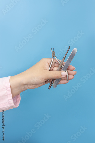 Woman holds manicure tools on blue background