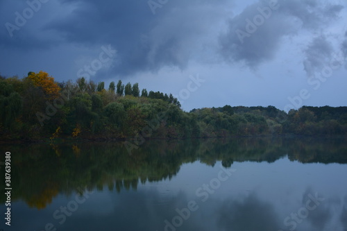 The trees above the water in a light evening fog after a slight autumn rain.
