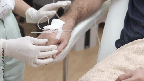 Close up of nurse or doctor preparing and adjusting infusion or chemotherapy drip for the male patient in hospital or beauty salon. Healthcare, wellness and medicine concept
