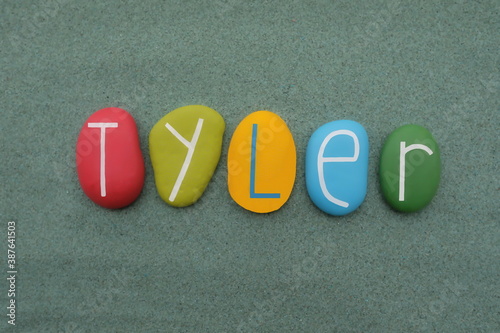 Tyler, given name composed with multicolored stone letters over green sand