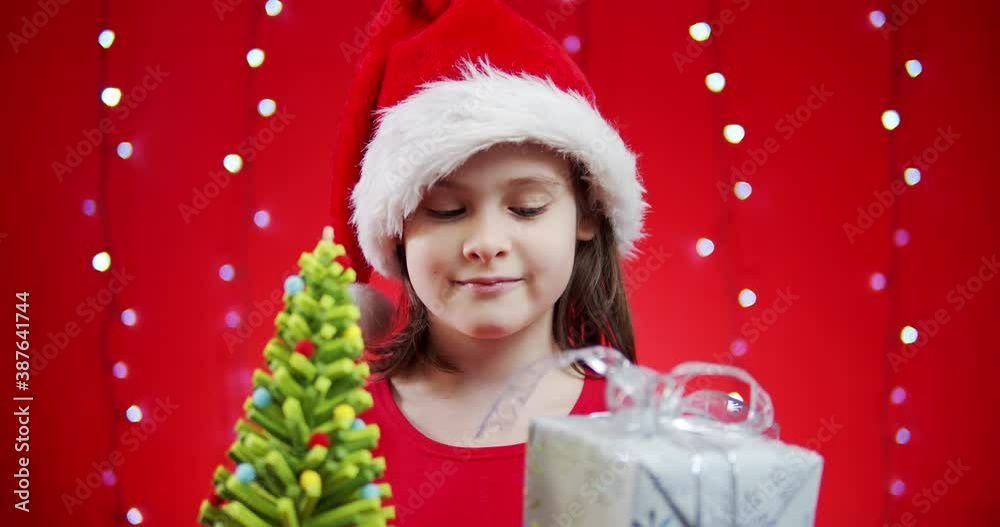cute girl in a santa hat holds a gift on a red christmas background cute girl in a santa hat holds a gift on a red christmas background
