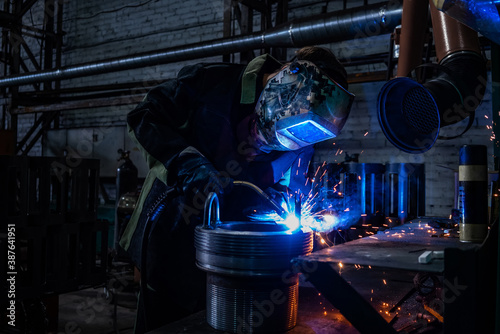 Side view of welder in protective helmet welding metal detail with sparks at factory photo