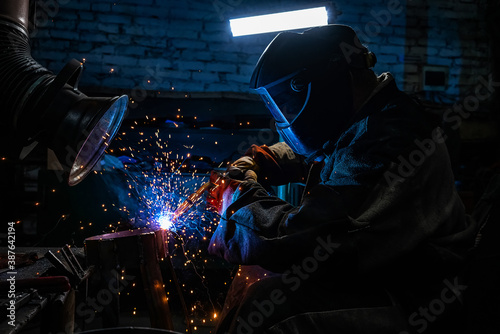 Side view of welder in protective helmet welding metal detail with sparks at factory