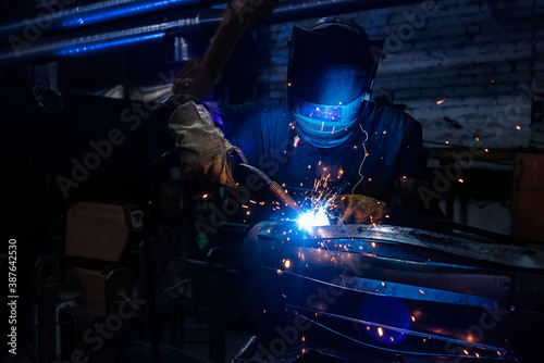 Side view of welder in protective helmet welding metal detail with sparks at factory