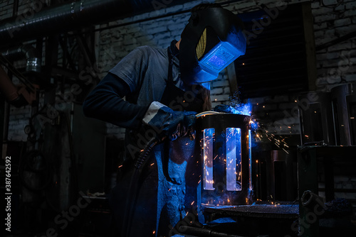 Side view of welder in protective helmet welding metal detail with sparks at factory © sutulastock
