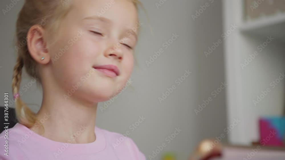 Tilt up closeup shot of cute elementary school girl with braided blonde hair using digital tablet and thinking or day dreaming at home Tilt up closeup shot of cute elementary school girl with braided blonde hair using digital tablet and thinking or day dreaming at home