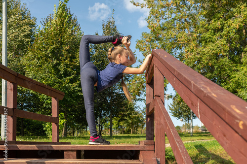 Ten year old caucasian girl doing yoga relaxation exercise on the top of wooden staircase in city park on sunny summer morning. Outdoor sport theme.
