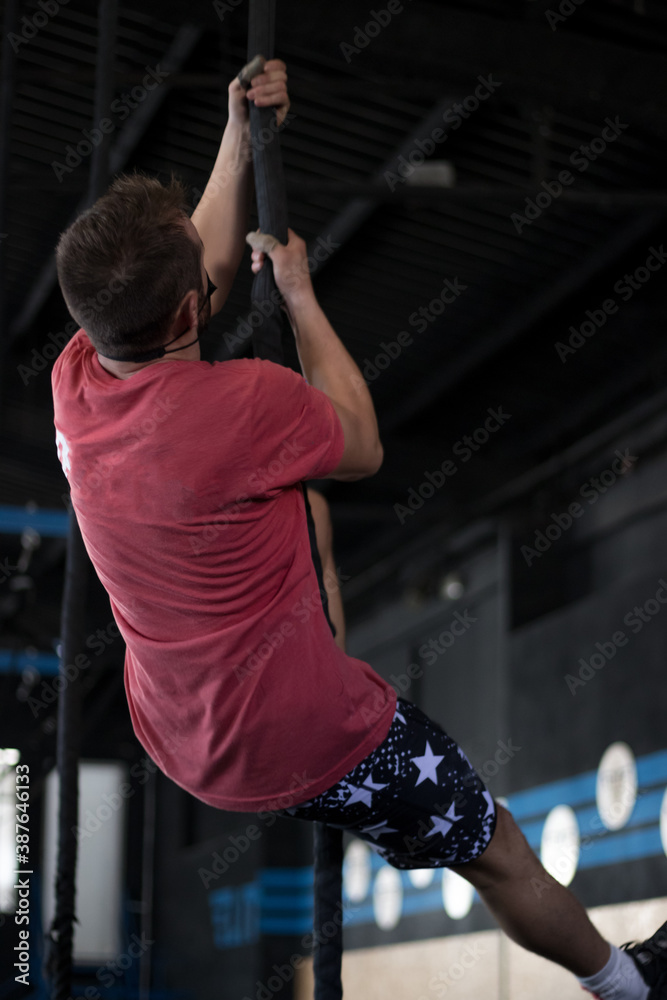 Fototapeta premium Chico con mascarilla en un gimnasio realizando Cross training, rope climb