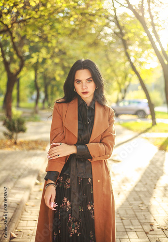 Fashionable elegant girl model walks along the street of the autumn city in park on a sunny day