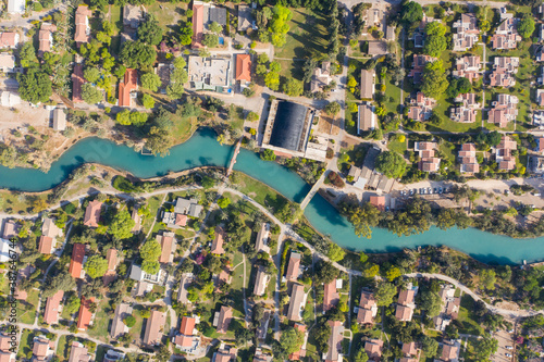 Aerial pass over Kibbutz Nir David with Asi river channel turquoise water dividing east and west side riverside houses and palm trees, Israel. photo