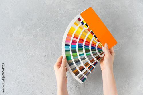 What color to paint the walls concept. Female hands holding a ral colors palette fan on a concrete background. Copy space. photo