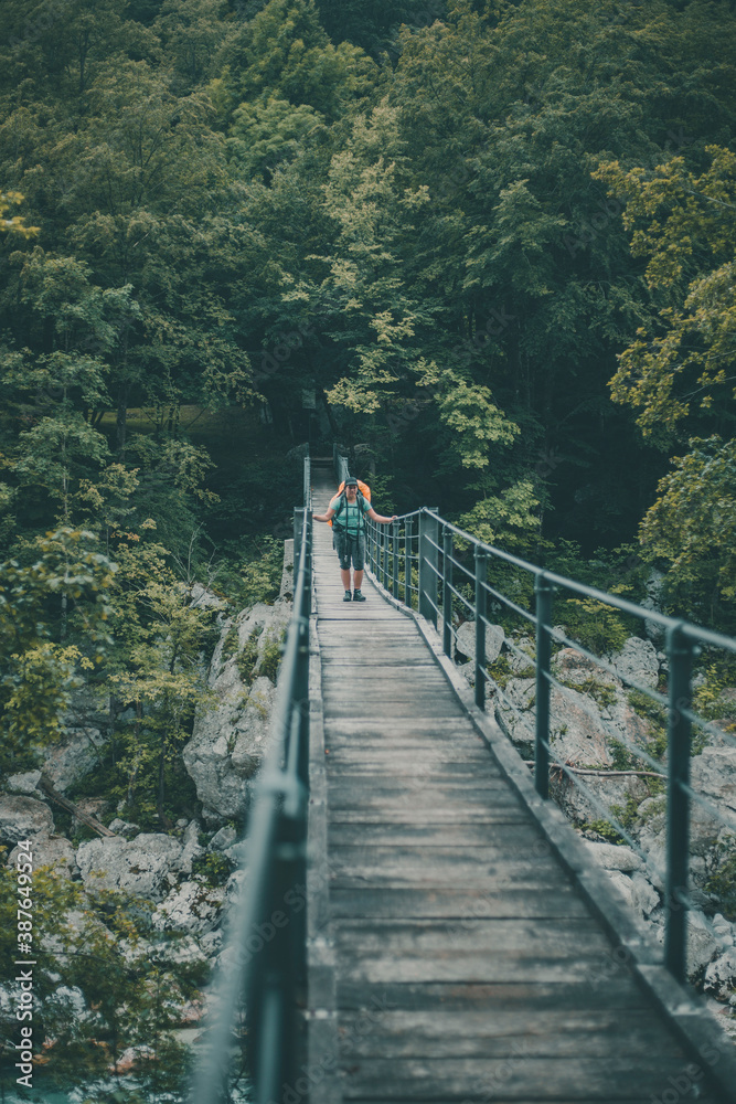 Young female backpacker trekking over a suspension bridge over the river Soča in Slovenia