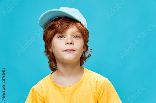 Red-haired boy with freckles with a cap on his head turned on the side yellow t-shirt 