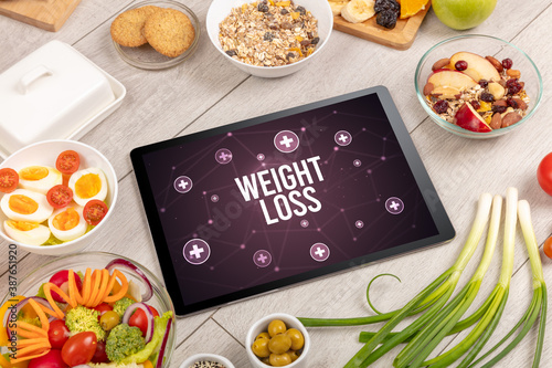 WEIGHT LOSS concept in tablet pc with healthy food around, top view