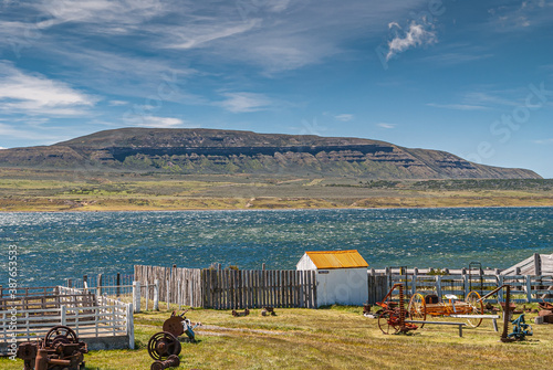 Riesco Island, Chile - December 12, 2008: Posada Estancia Rio Verde working farm. Landscape over Otway sound showing mountain with natural balcony lines under blue cloudscape. Agriculture machinery up photo