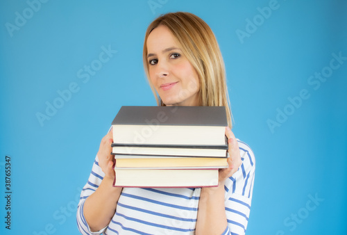 Isolated young happy beautiful woman holding books over blue background.