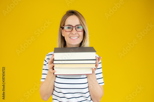 Isolated young happy beautiful woman holding books over yellow background.