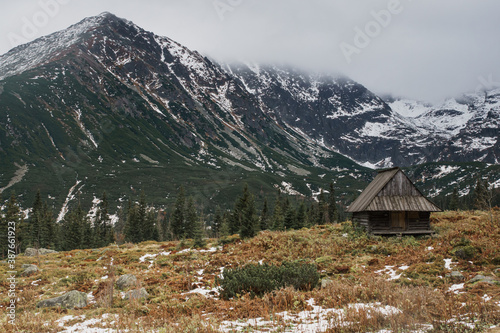 Obraz na płótnie Old wooden cottage among high mountains, fiords landscape, with fog and snow all around. Concept of isolation, social distance travel, trekking in Europe. Moody, desaturated colors. w salonie