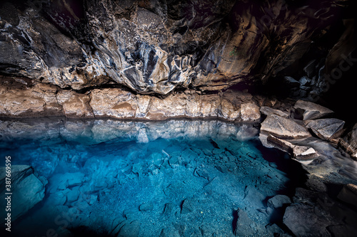 Inside of dark Grjotagja lava cave near lake Myvatn with hot springs blue water and rocks, rocky formations on walls reflection