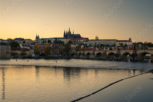 view of the Vltava river and Prague Castle St. Vitus Cathedral and Charles Bridge in the center of Prague at sunset. there are reflections on the river surface and the sky is illuminated by the sun