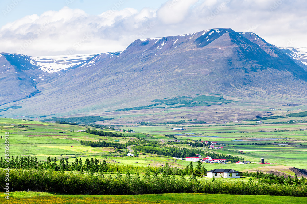 View of Sulur mountains near Akureyri with blue sky clouds and pasture farm pastoral landscape with green grass during summer day View of Sulur mountains near Akureyri with blue sky clouds and pasture farm pastoral landscape with green grass during summer day