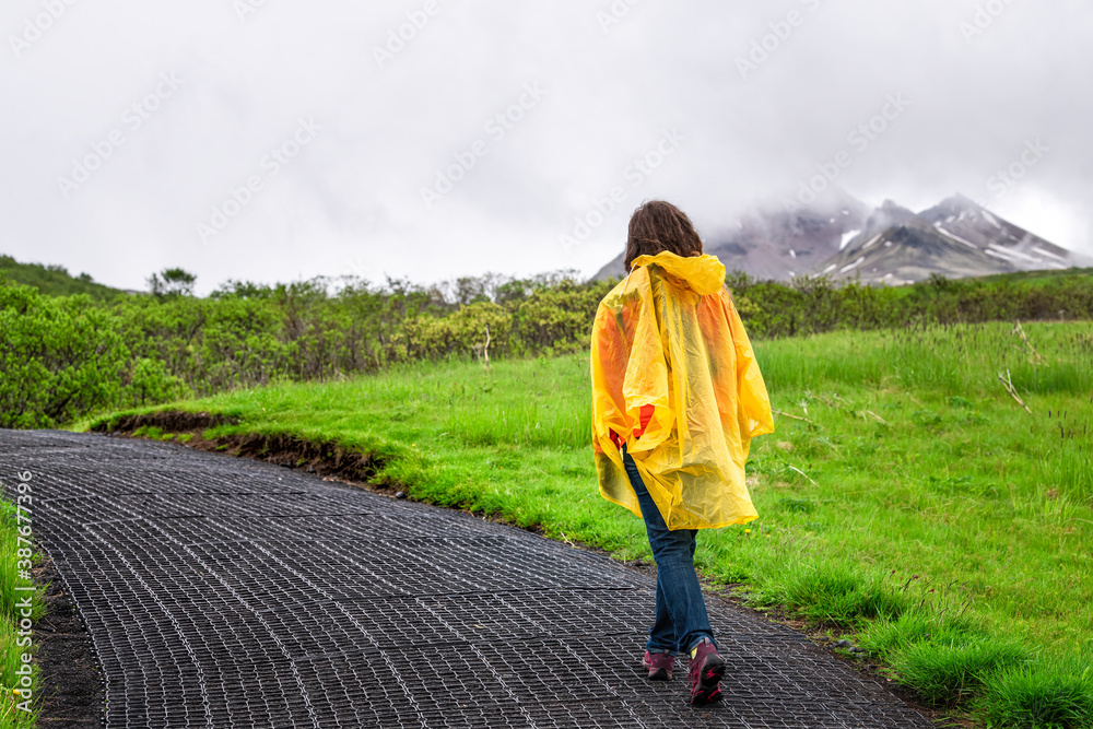 Skaftafell, Iceland green summer landscape and woman in yellow poncho walking hiking on wet trail path hiking road and cloudy sky with mountains