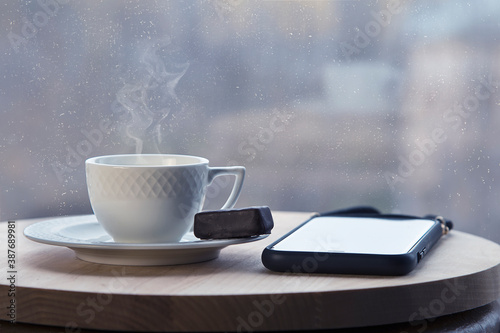 Coffee cup with smoke, cellphone on wooden table in cafe