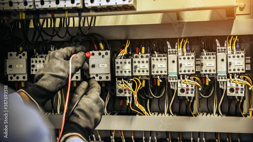Electrical engineer using measuring equipment to checking electric current voltage at circuit breaker and cable wiring system for maintenance in main power distribution board.