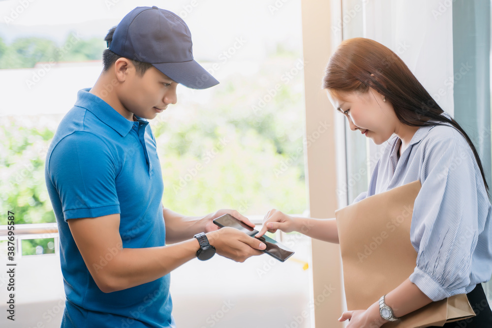 Obraz premium Asian deliveryman delivering package box parcel giving to female customer signing using smart technology tablet at home delivery service logistics business ordering mail posting front door of house