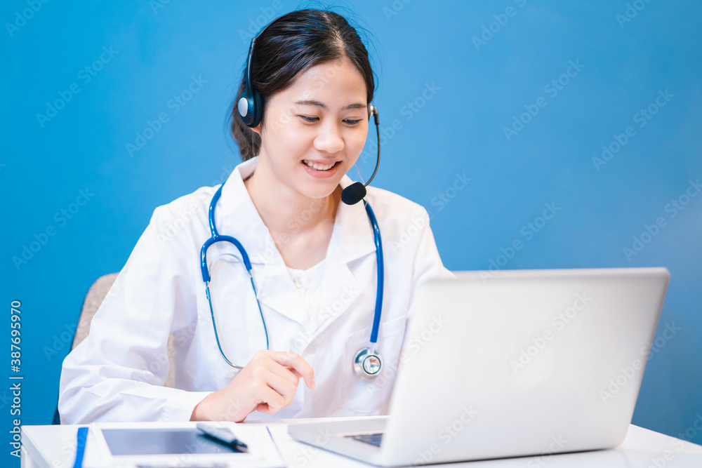Medical healthcare Asian female attractive doctor using computer laptop technology video calling communicating headset diagnosing meeting with patients in hospital office blue isolated background Medical healthcare Asian female attractive doctor using computer laptop technology video calling communicating headset diagnosing meeting with patients in hospital office blue isolated background