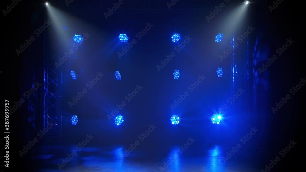 Blue moving light and white rays on an empty stage in the dark. Stage