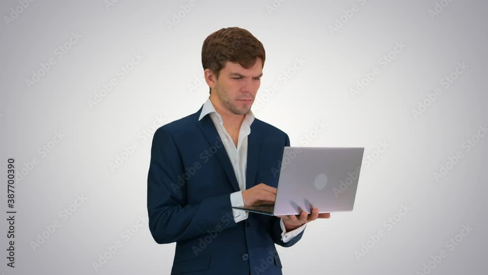 Concentrated young businessman working on laptop while standing on gradient background. Concentrated young businessman working on laptop while standing on gradient background.