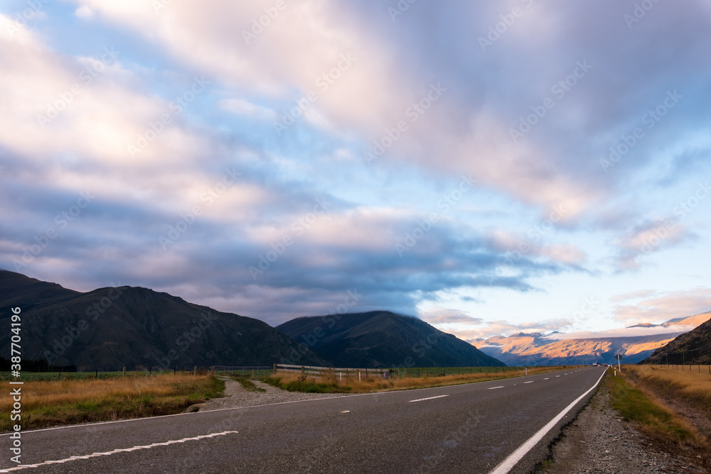 Naklejka premium A long straight road with raining cloud and Mountain in evening