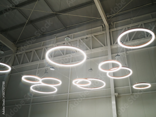 White circular ring shaped lamps hang under a concrete ceiling with external wiring