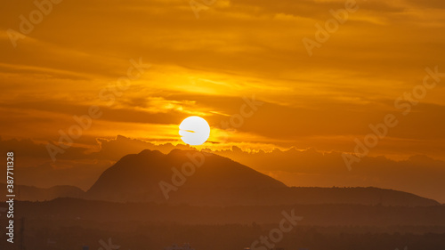Silhouette of a hill against beautiful golden hour light and beautiful clouds formation in the horizon with the sun setting 