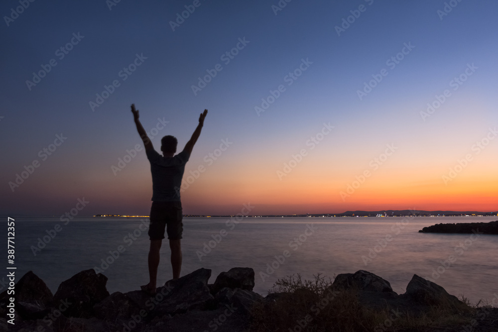 Silhouette of a man greeting the sunset by the sea