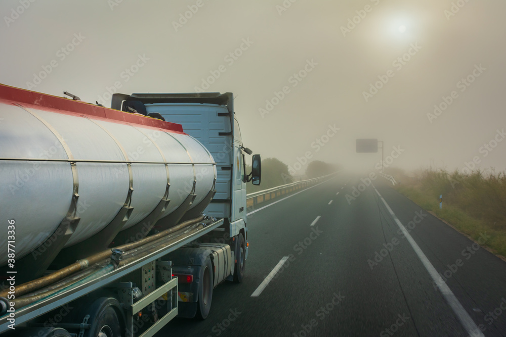 Tank truck driving on a highway with poor visibility due to fog.