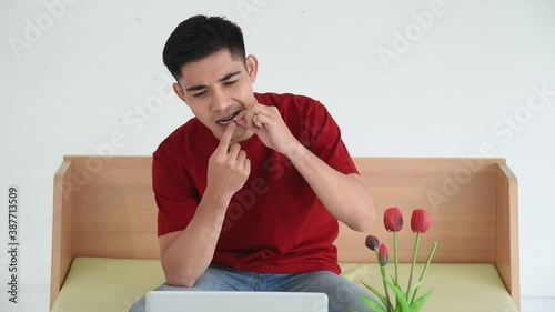 Young Asian man wear braces in casual outfit using laptop for video call or facetime with dentist and explaining toothache