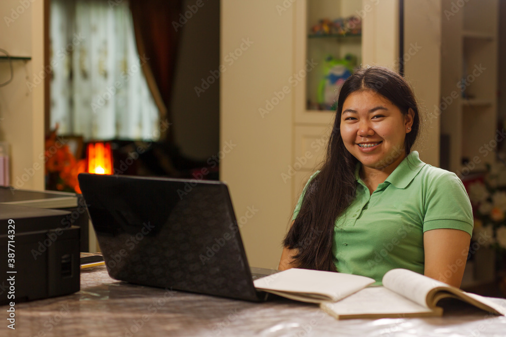 Asian student girl smiling to camera while studying at home, using laptop computer and have a short note on table Asian student girl smiling to camera while studying at home, using laptop computer and have a short note on table