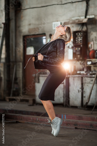 Blonde girl wearing leather jacket and a stretched mini dress in an old spooky factory