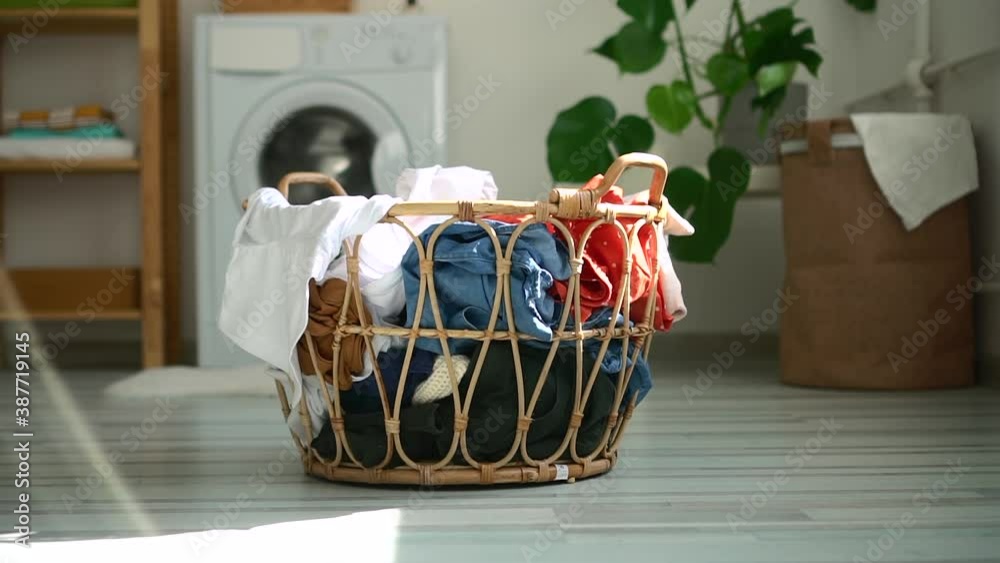 Basket of dirty clothes is standing on floor in laundry room at home spbd. Close-up view of container filled with clothing stands on background of washing machine indoors. Picture of house during