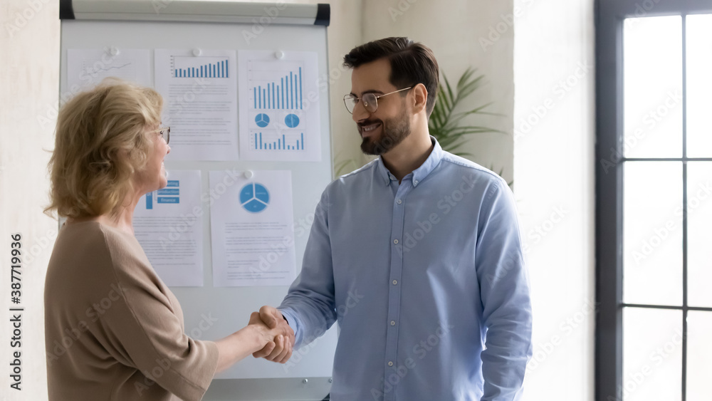Obraz premium Smiling businessman shake hand of middle-aged female employee greeting with job success or promotion. Happy male CEO handshake woman worker or partner get acquainted in office. Employment concept.