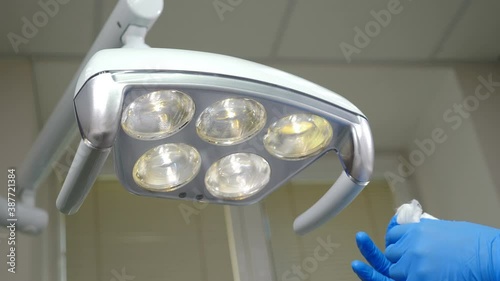 Cleaning medical lamp in dental clinic, operating medical facility in cabinet. Clinic Hygiene Concept. Sterilization and disinfection, Preparing dental cabinet office before treating patient. 4 k