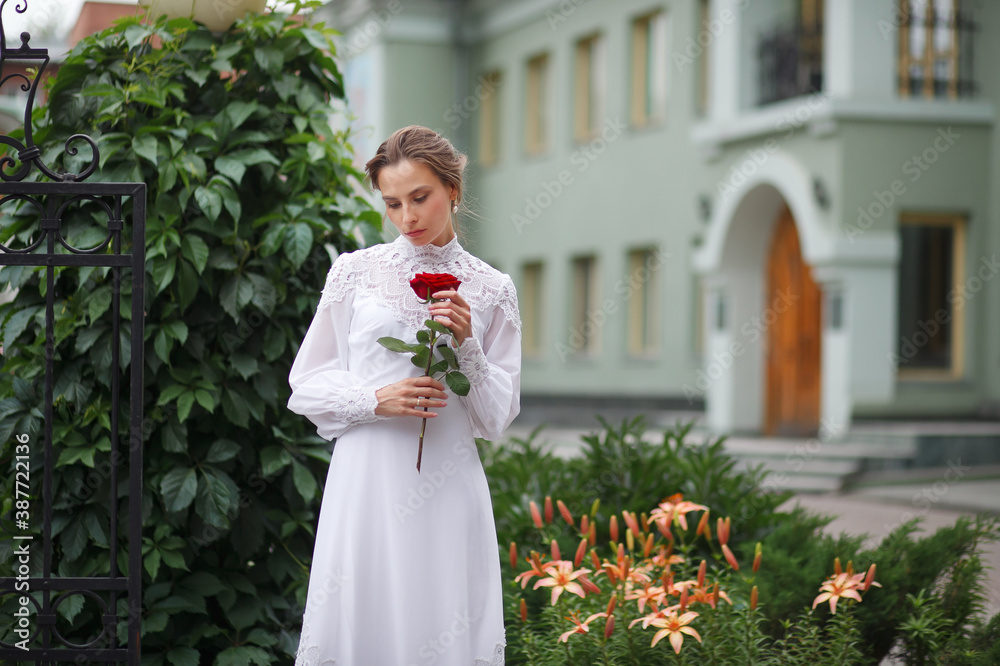 Fototapeta premium beautiful girl in a vintage dress walks in the garden, bride with a red rose in her hands