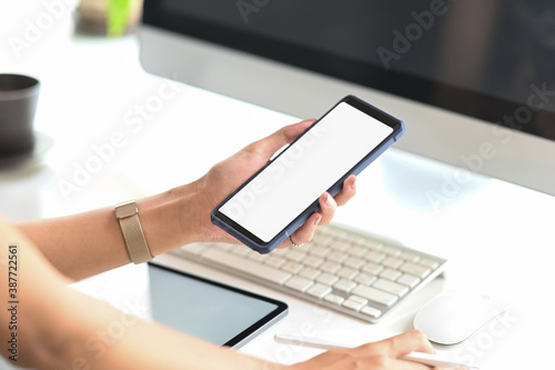 Cropped image of businesswoman using mockup cellphone gadget with blank screen on her work space.