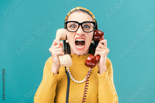 Woman holding two telephone receivers and shouting photo