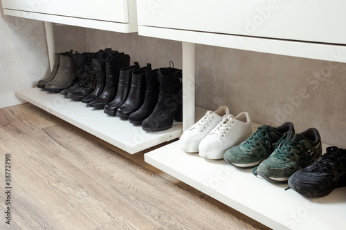 Organized shoe rack, shoe rack with black stylisch shoes and boots, on a wooden floor, besides a white wall. modern room