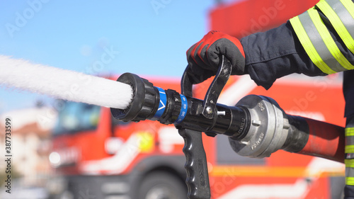 A fireman keeps fire hose and extinguishes fire for training. Fire station background.