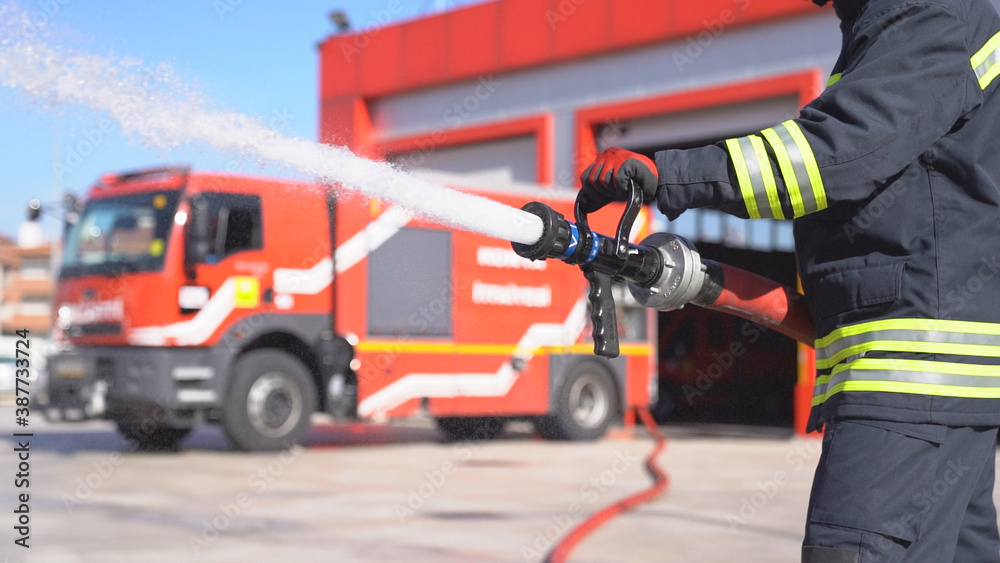 A fireman keeps fire hose and extinguishes fire for training. Fire station background.
